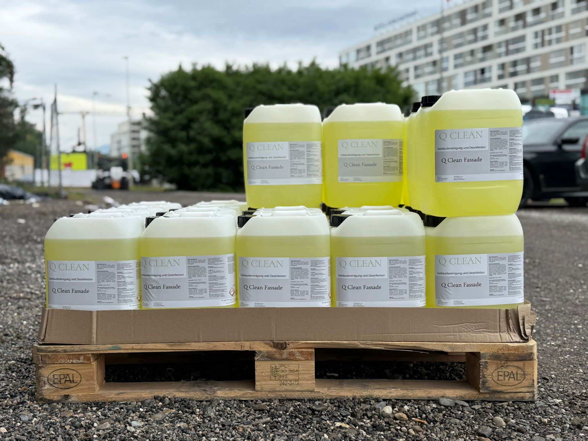 Mehrere gelbe Q Clean Fassadenreiniger Kanister auf einer Europalette im Freien gestapelt