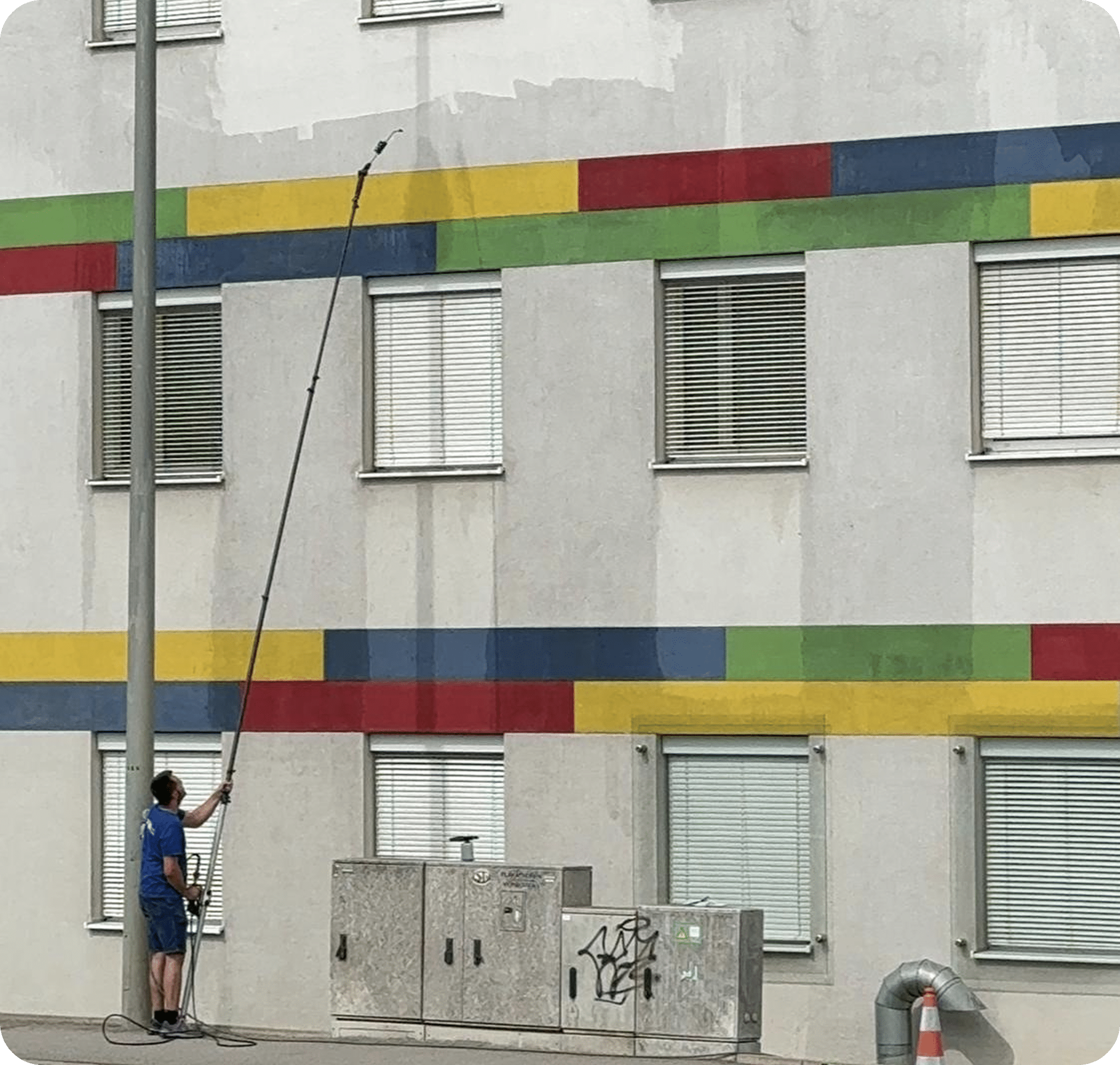 Reinigungskraft säubert mehrfarbige Gebäudefassade mit langem Teleskopstab – QClean Fassadenreinigung
